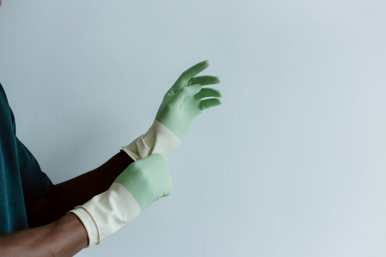 Close-up of a person putting on green latex cleaning gloves over a blue background.